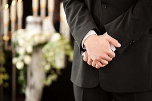 Mies kädet ristissä hautajaisissa