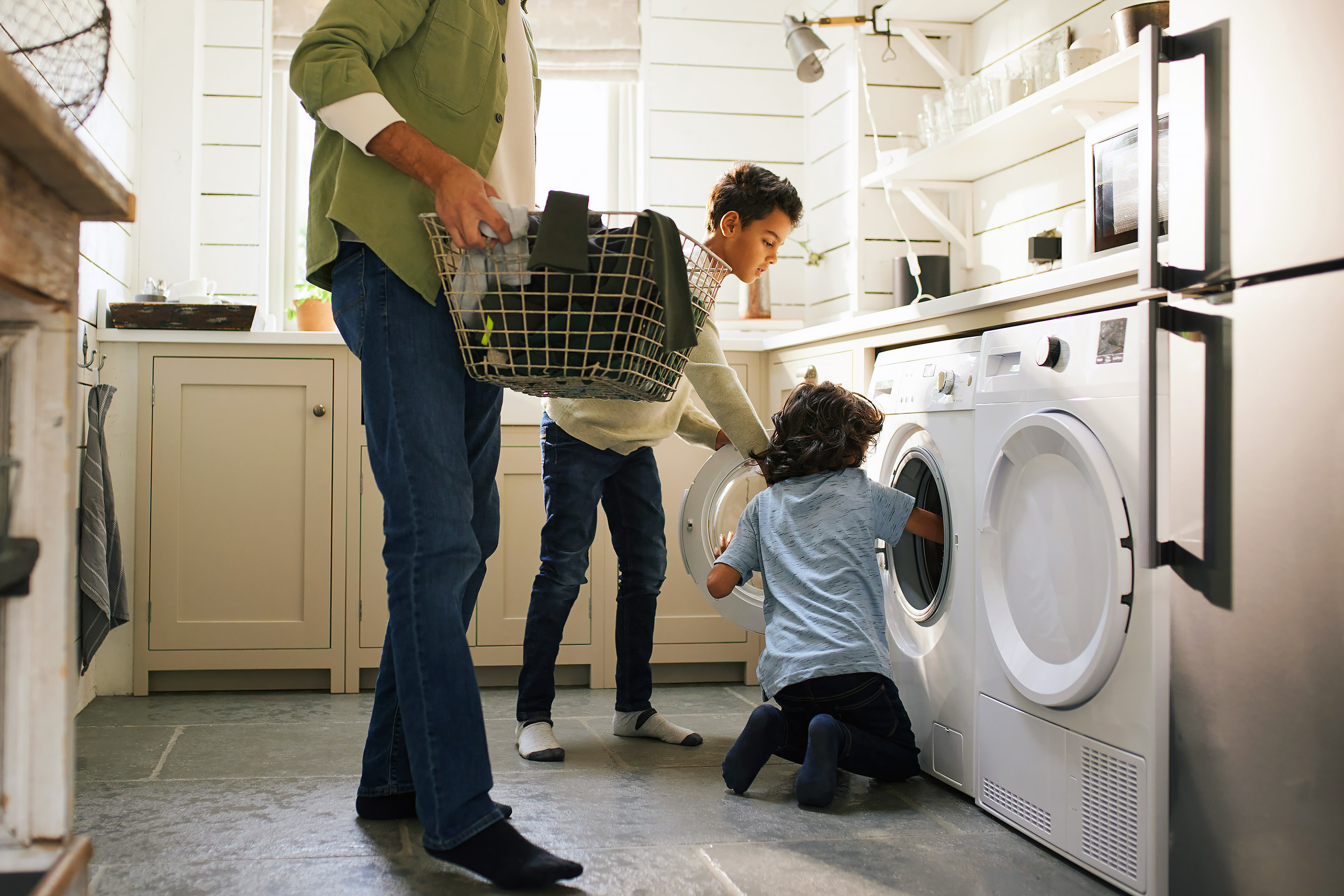 Kaksi poikaa auttavat isäänsä pyykkikoneen tyhjennyksessä.